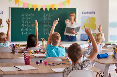 young children in a classroom raising their hands