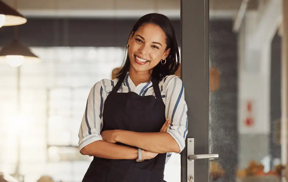shop-owner-wide-iStock-1400817945 photo of a smiling female business owner standing at the door to her shop